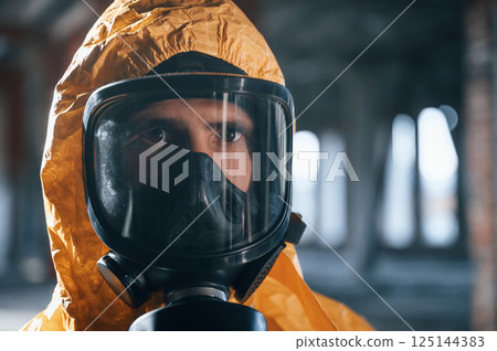Portrait of man dressed in chemical protection suit that is in the ruins of the post apocalyptic building 125144383