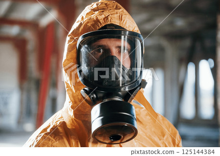 Portrait of man dressed in chemical protection suit that is in the ruins of the post apocalyptic building 125144384