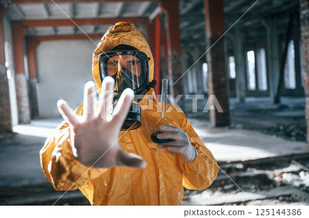 Stop sign by hand. Man dressed in chemical protection suit in the ruins of the post apocalyptic building 125144386