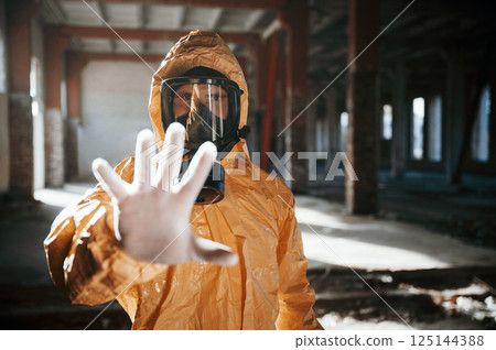 Stop sign by hand. Man dressed in chemical protection suit in the ruins of the post apocalyptic building Stop sign by hand. Man dressed in chemical protection suit in the ruins of the post apocalyptic building 125144388
