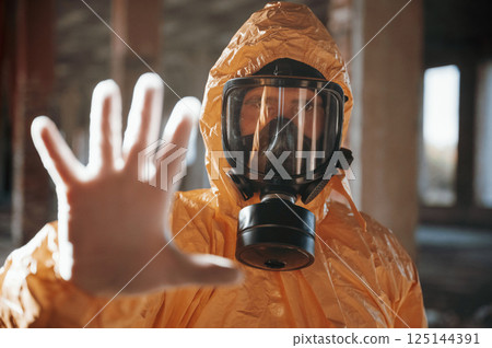 Stop sign by hand. Man dressed in chemical protection suit in the ruins of the post apocalyptic building 125144391