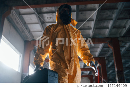 Walking with hard case. Man dressed in chemical protection suit in the ruins of the post apocalyptic building Walking with hard case. Man dressed in chemical protection suit in the ruins of the post apocalyptic building 125144409