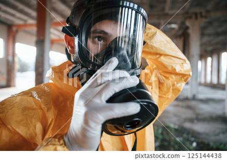 Wearing the respirator. Man dressed in chemical protection suit in the ruins of the post apocalyptic building 125144438