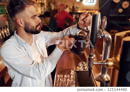 Side view. Bartender pours beer. Man is working in the bar Side view. Bartender pours beer. Man is working in the bar 125144490