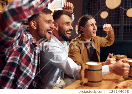 Watching TV. Three friends are in the bar drinking beer and having a good time 125144658