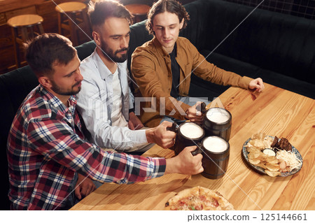 Knocking the mugs. Three friends are in the bar drinking beer and having a good time 125144661
