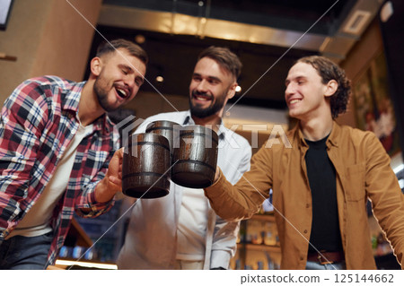 Knocking the mugs. Three friends are in the bar drinking beer and having a good time 125144662