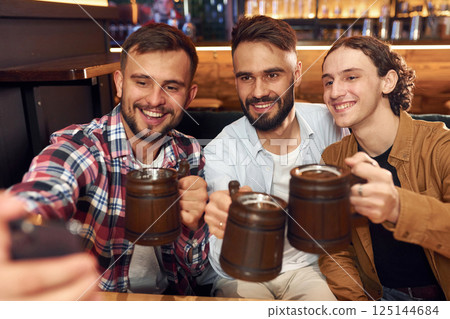 Making selfie. Three friends are in the bar drinking beer and having a good time Making selfie. Three friends are in the bar drinking beer and having a good time 125144684