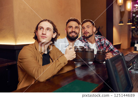 Sitting and smiling. Three friends are in the bar drinking beer and having a good time 125144689