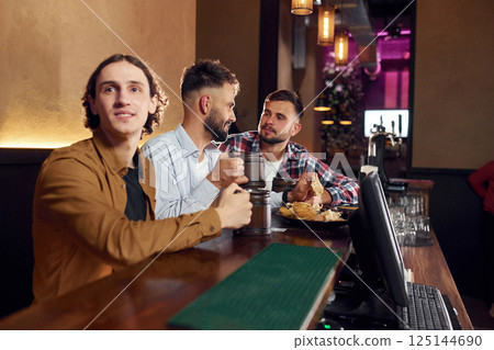 Three friends are in the bar drinking beer and having a good time 125144690