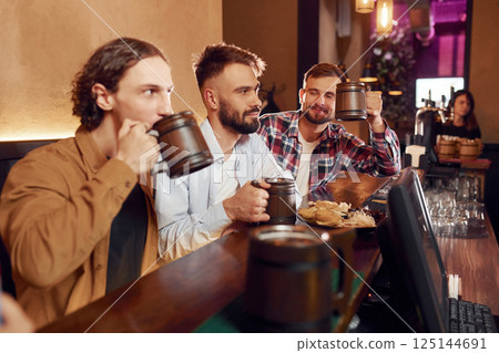 Three friends are in the bar drinking beer and having a good time Three friends are in the bar drinking beer and having a good time 125144691