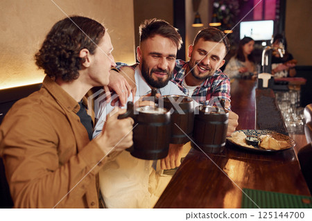 Sitting by the table. Three friends are in the bar drinking beer and having a good time 125144700