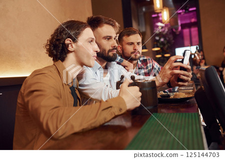 Sitting by the table. Three friends are in the bar drinking beer and having a good time 125144703