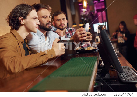 Sitting by the table. Three friends are in the bar drinking beer and having a good time 125144704