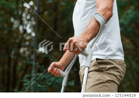 Close up view. Man with crutches is in the park outdoors. Having leg injury Close up view. Man with crutches is in the park outdoors. Having leg injury 125144819