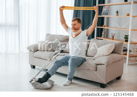 Rehabilitation exercises for arms. Man with crutches is at home indoors. Having injuries Rehabilitation exercises for arms. Man with crutches is at home indoors. Having injuries 125145488