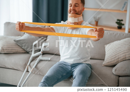 Rehabilitation exercises for arms. Man with crutches is at home indoors. Having injuries 125145490