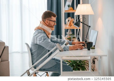 Working from home by using laptop. Man with crutches is indoors. Having injuries 125145505