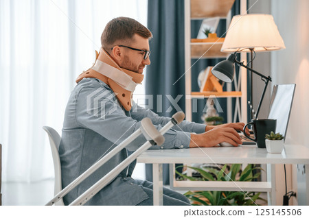 Working from home by using laptop. Man with crutches is indoors. Having injuries 125145506