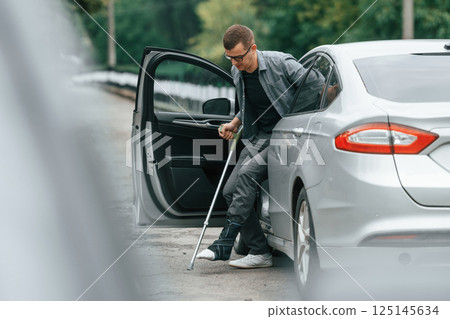 Injured man with crutches is going out from the car 125145634