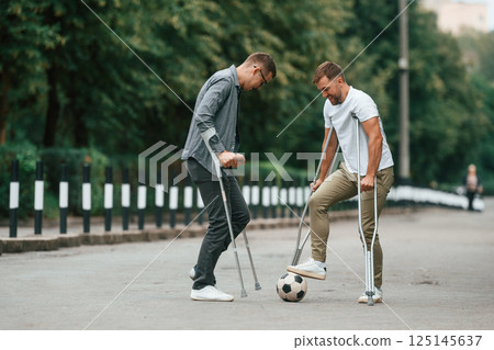 Playing soccer. Two men with crutches is outdoors on the road 125145637