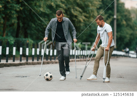 Playing soccer. Two men with crutches is outdoors on the road 125145638