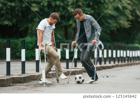Having fun, playing soccer. Two men with crutches is outdoors on the road 125145642