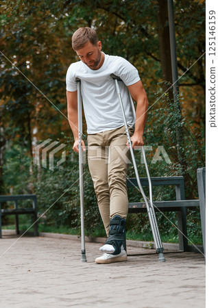 Standing and walking. Man with crutches is in the park outdoors. Having leg injury 125146159