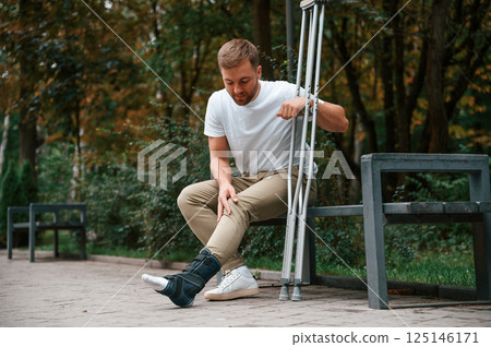 Looking at the broken leg. Man with crutches is in the park outdoors. Having leg injury 125146171