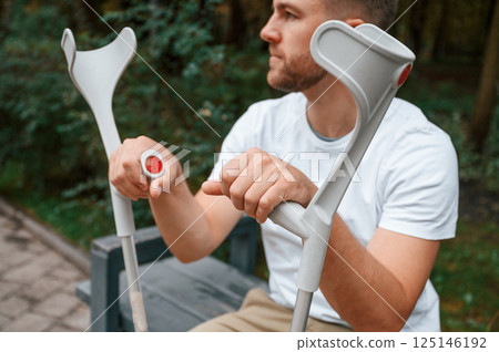 Sitting with crutches. Man is in the park outdoors. Having leg injury Sitting with crutches. Man is in the park outdoors. Having leg injury 125146192