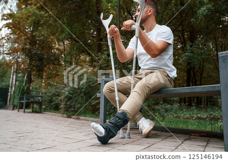 Sitting with crutches. Man is in the park outdoors. Having leg injury 125146194