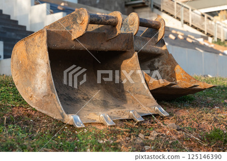 Rusty digger attachments on the ground at a home building site. Mini excavator and terrain work in progress with fresh red soil and stepped concrete structures. High quality photo Rusty digger attachments on the ground at a home building site. Mini excavator and terrain work in progress with fresh red soil and stepped concrete structures. High quality photo 125146390