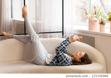 Teenage girl lying on sofa using smartphone at home. 125146966
