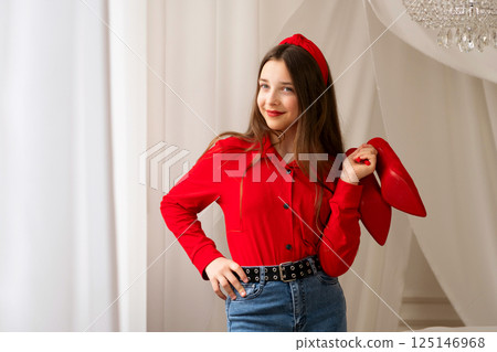 Smiling teen girl posing with red high heels indoors. 125146968