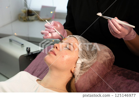 Professional applies rejuvenating face mask to client's forehead Professional applies rejuvenating face mask to client's forehead 125146977