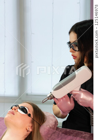 Esthetician adjusts handheld laser above client's eyebrow for removal 125146978