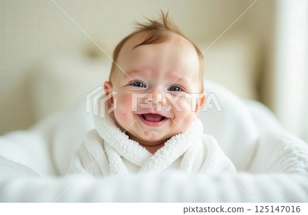 Happy laughing baby in white robe towel after bath or shower. Clean dry baby. Bathing and washing small children. Baby hygiene. Textiles for babies. 125147016