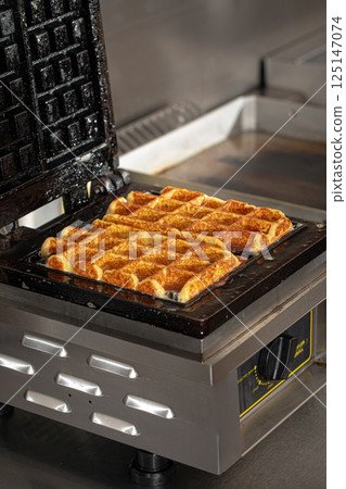 Cooking belgian waffles in the cafe kitchen Cooking belgian waffles in the cafe kitchen 125147074
