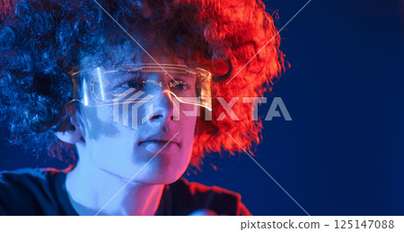 Futuristic eyewear. Young man with curly hair is indoors illuminated by neon lighting 125147088
