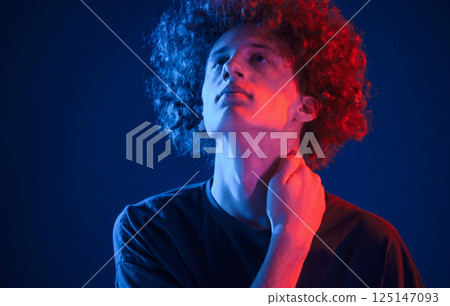 Looking up. Young man with curly hair is indoors illuminated by neon lighting 125147093