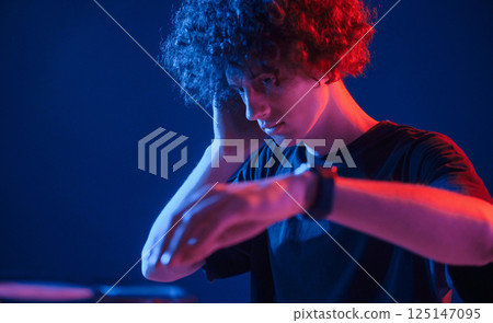 DJ is in the club. Young man with curly hair is indoors illuminated by neon lighting DJ is in the club. Young man with curly hair is indoors illuminated by neon lighting 125147095