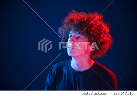 Looking up. Young man with curly hair is indoors illuminated by neon lighting Looking up. Young man with curly hair is indoors illuminated by neon lighting 125147113