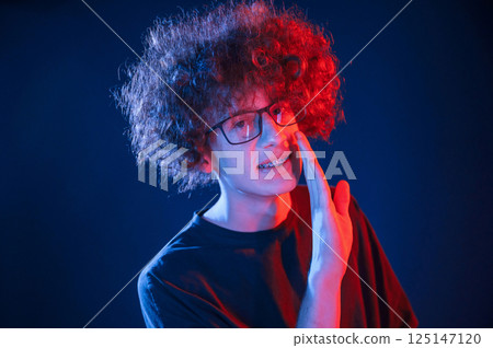 Conception of gossip. Telling a secret. Young man with curly hair is indoors illuminated by neon lighting 125147120