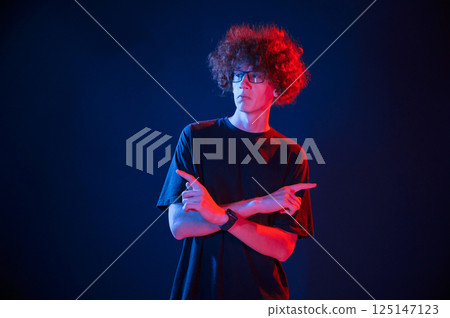 Posing for the camera. Young man with curly hair is indoors illuminated by neon lighting Posing for the camera. Young man with curly hair is indoors illuminated by neon lighting 125147123