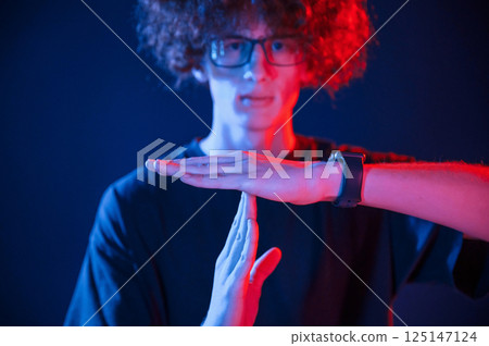 Hands gesture. Young man with curly hair is indoors illuminated by neon lighting Hands gesture. Young man with curly hair is indoors illuminated by neon lighting 125147124