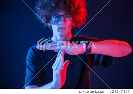 Hands gesture. Young man with curly hair is indoors illuminated by neon lighting Hands gesture. Young man with curly hair is indoors illuminated by neon lighting 125147125