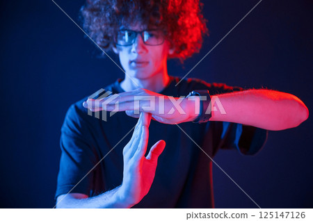 Hands gesture. Young man with curly hair is indoors illuminated by neon lighting Hands gesture. Young man with curly hair is indoors illuminated by neon lighting 125147126