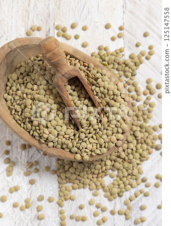 Bowl full of dried raw green lentils with a wooden scoop on white table top view. Vegetarian food 125147558