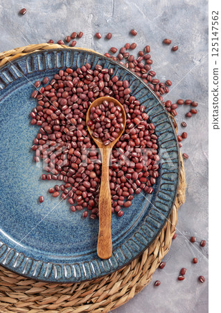 Blue plate full of dried red azuki beans with a wooden spoon top view. Vegetarian protein source 125147562