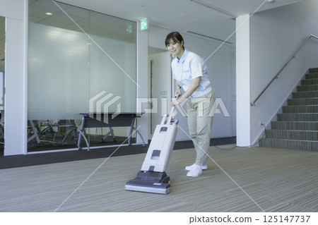一名年輕的女清潔工正在吸塵辦公大樓的地板。照片提供：東京電子專門學校、電波學園 125147737